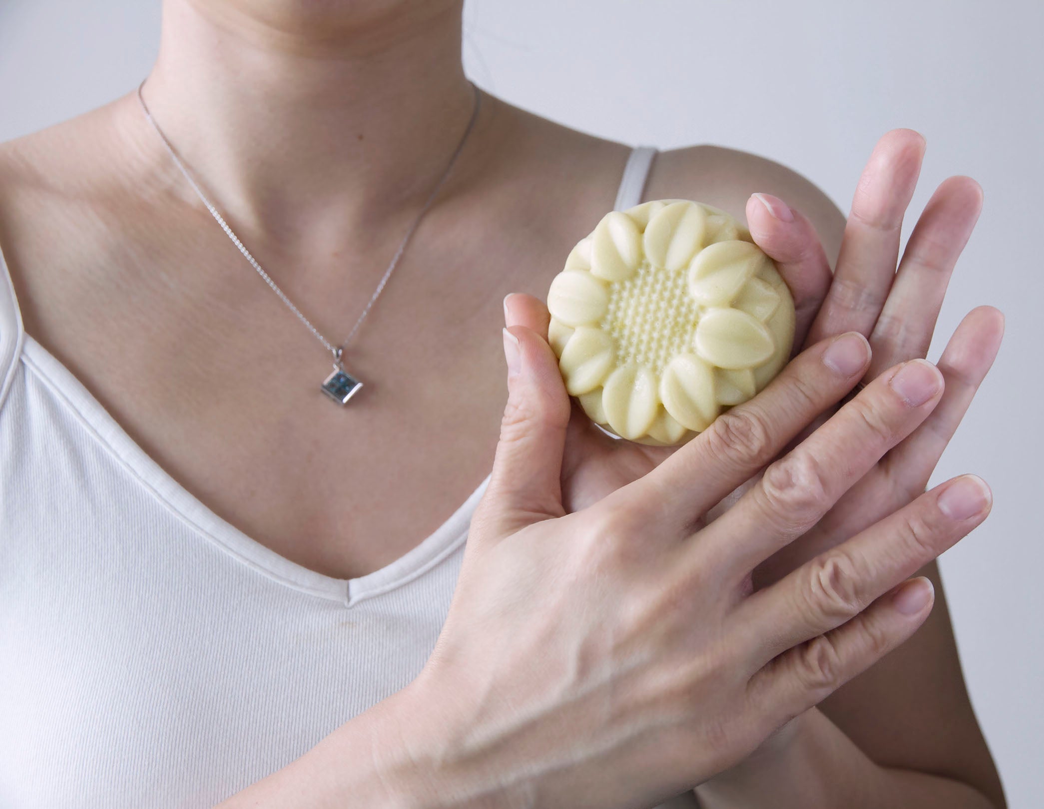Person holding a round, flower-shaped lotion bar in their hand